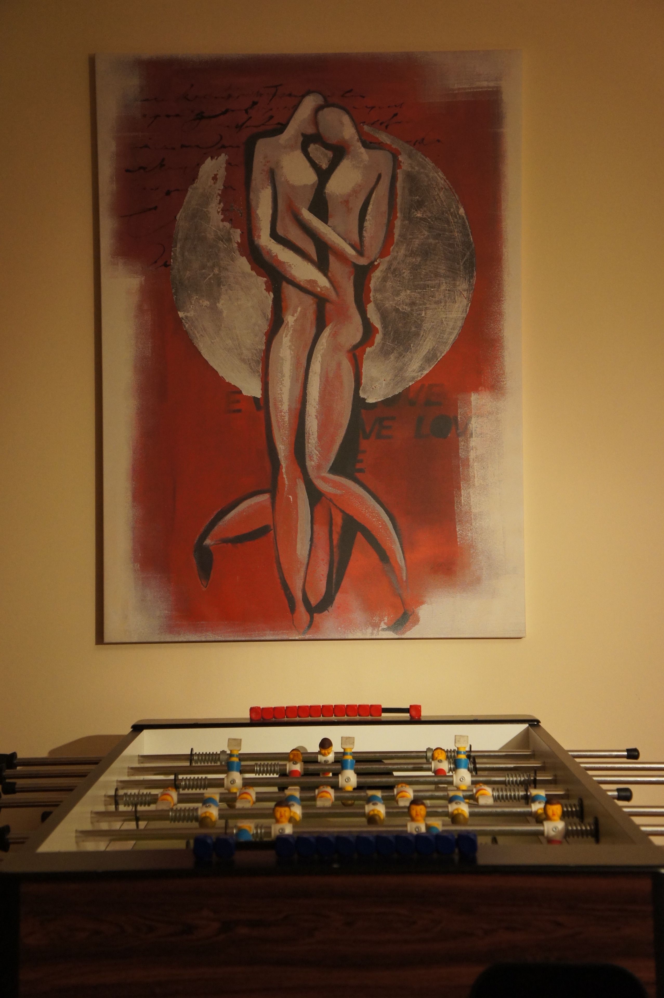 Quarto com mesa de futebol e uma grande pintura abstrata na parede.