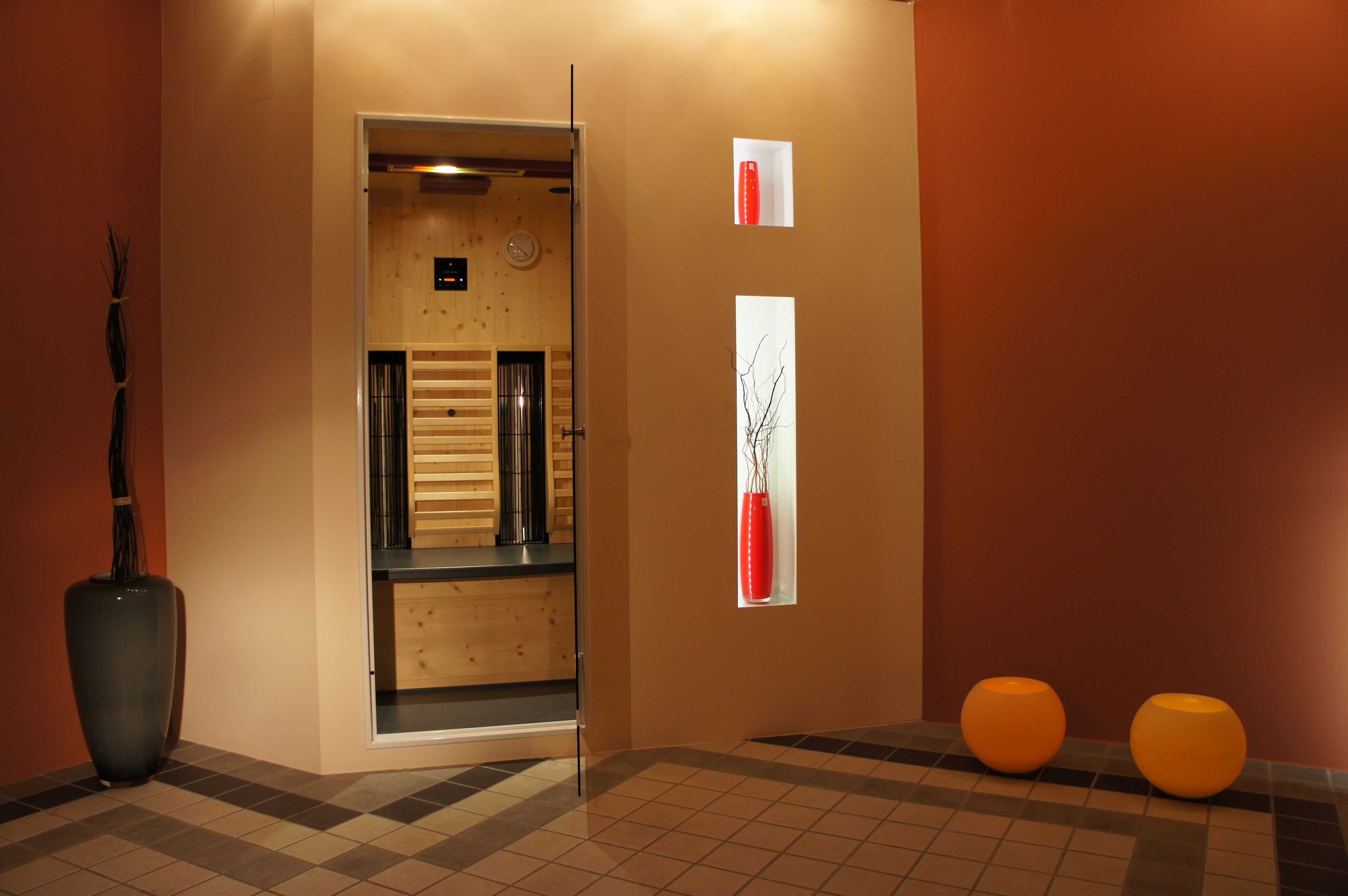 A hallway with a wooden door, a large vase, and two orange stools.