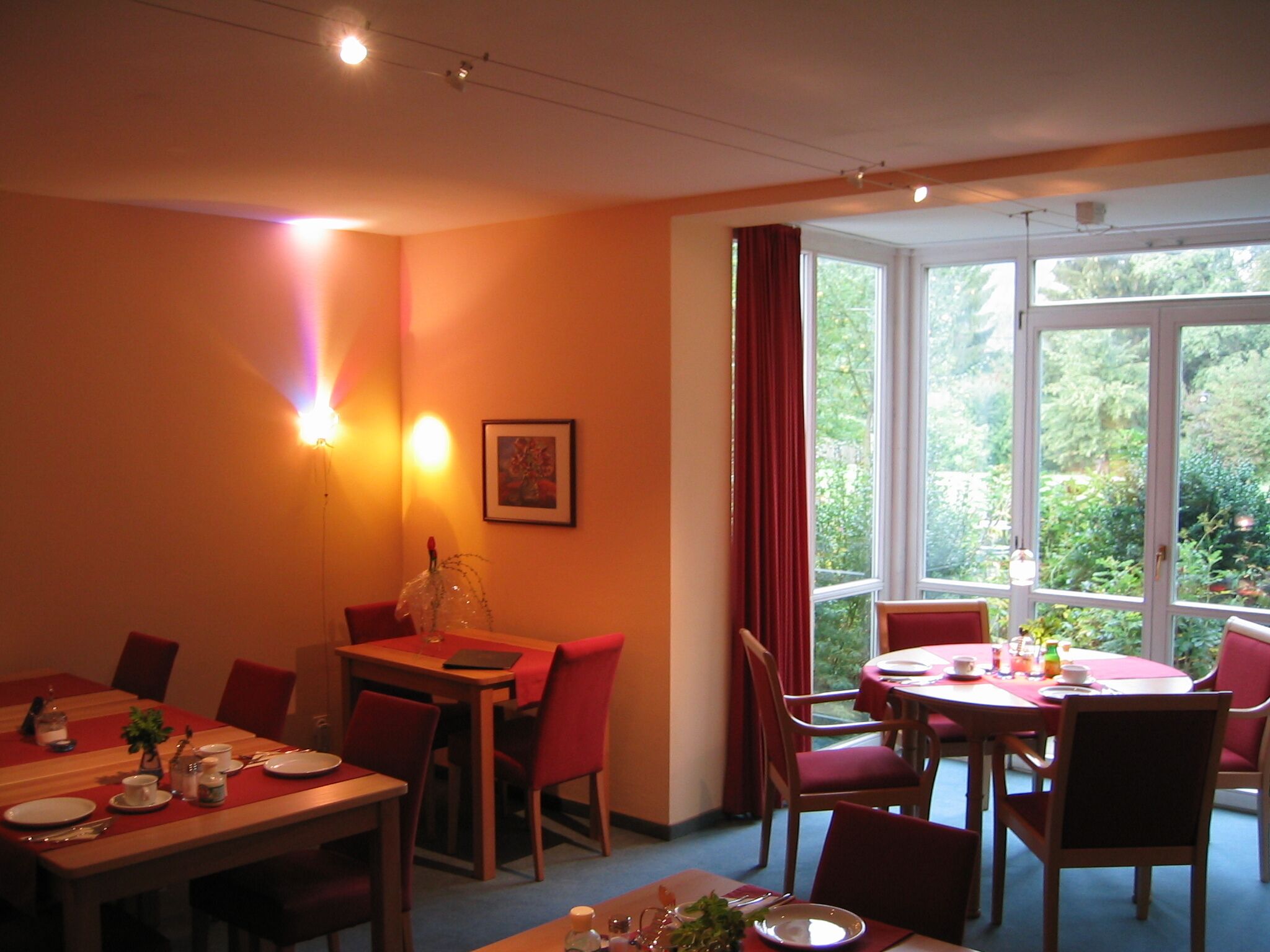 A dining area with a table set for four, red chairs, and a window with a view of greenery.