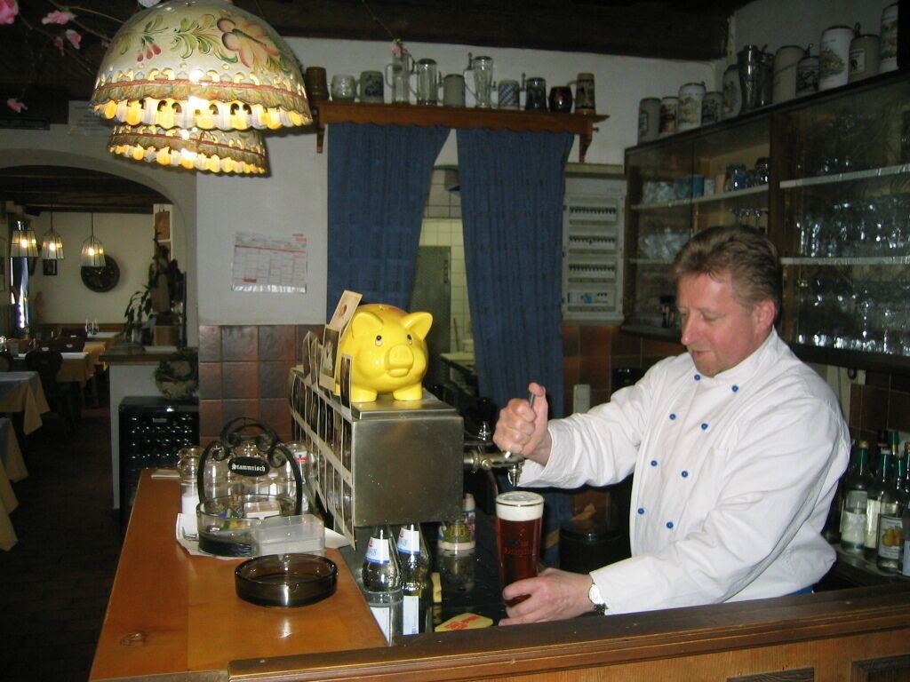 A bar area with a bartender pouring a drink, a piggy bank, and shelves with glassware.