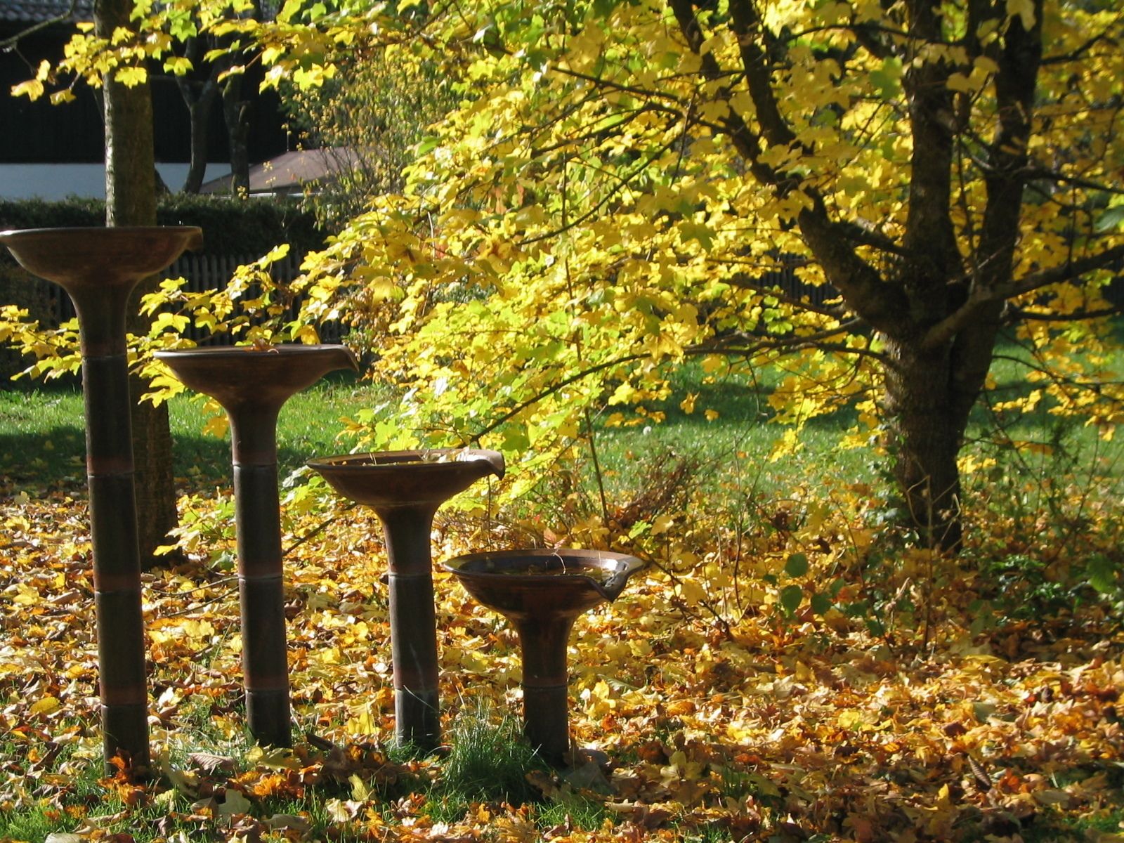 Tres esculturas de jardín al aire libre, con un árbol y hojas otoñales de fondo.