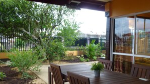 Un patio con mesa y sillas de madera, rodeado de plantas y una valla.