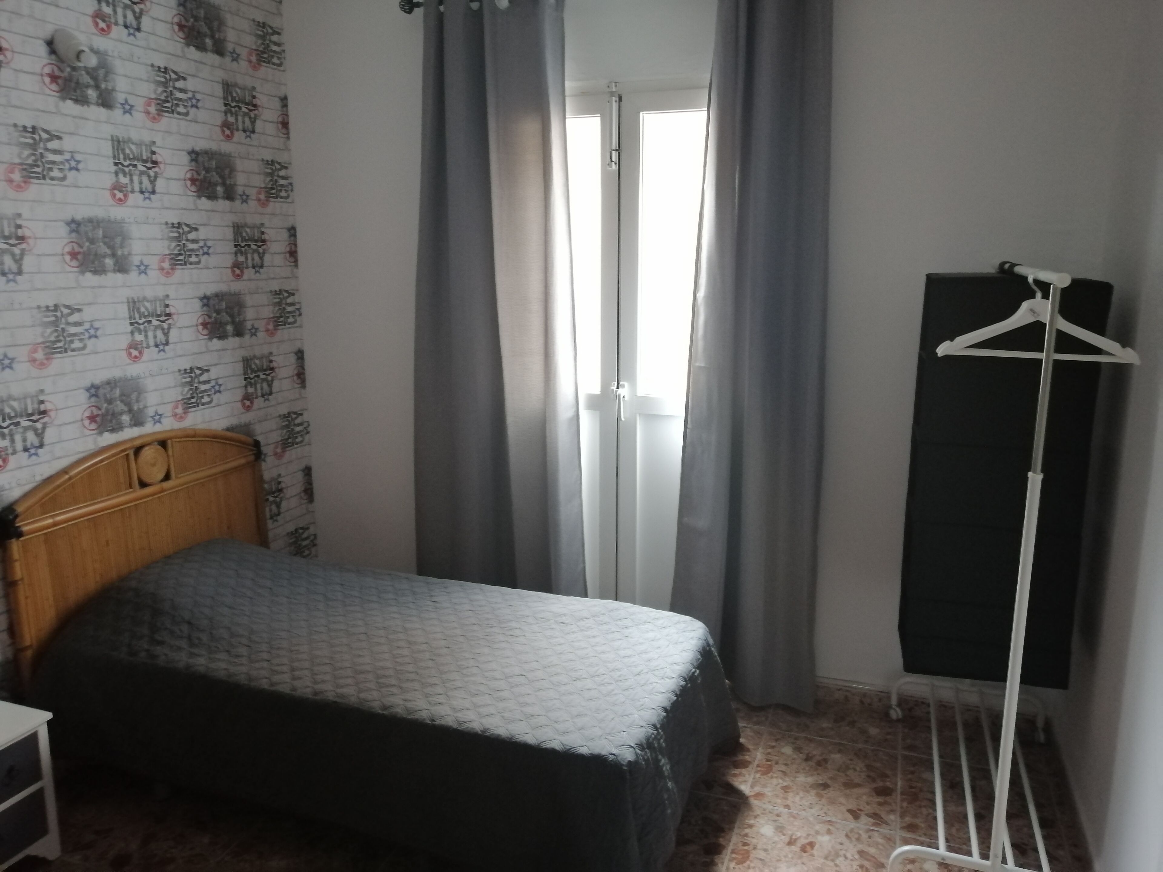 Un dormitorio con cama, armario, perchero y ventana con cortinas.