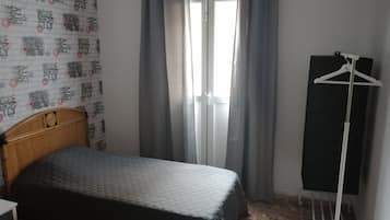 Un dormitorio con cama, armario, perchero y ventana con cortinas.