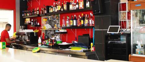Angolo bar con scaffali di bottiglie di liquore, un orologio e un monitor computer.