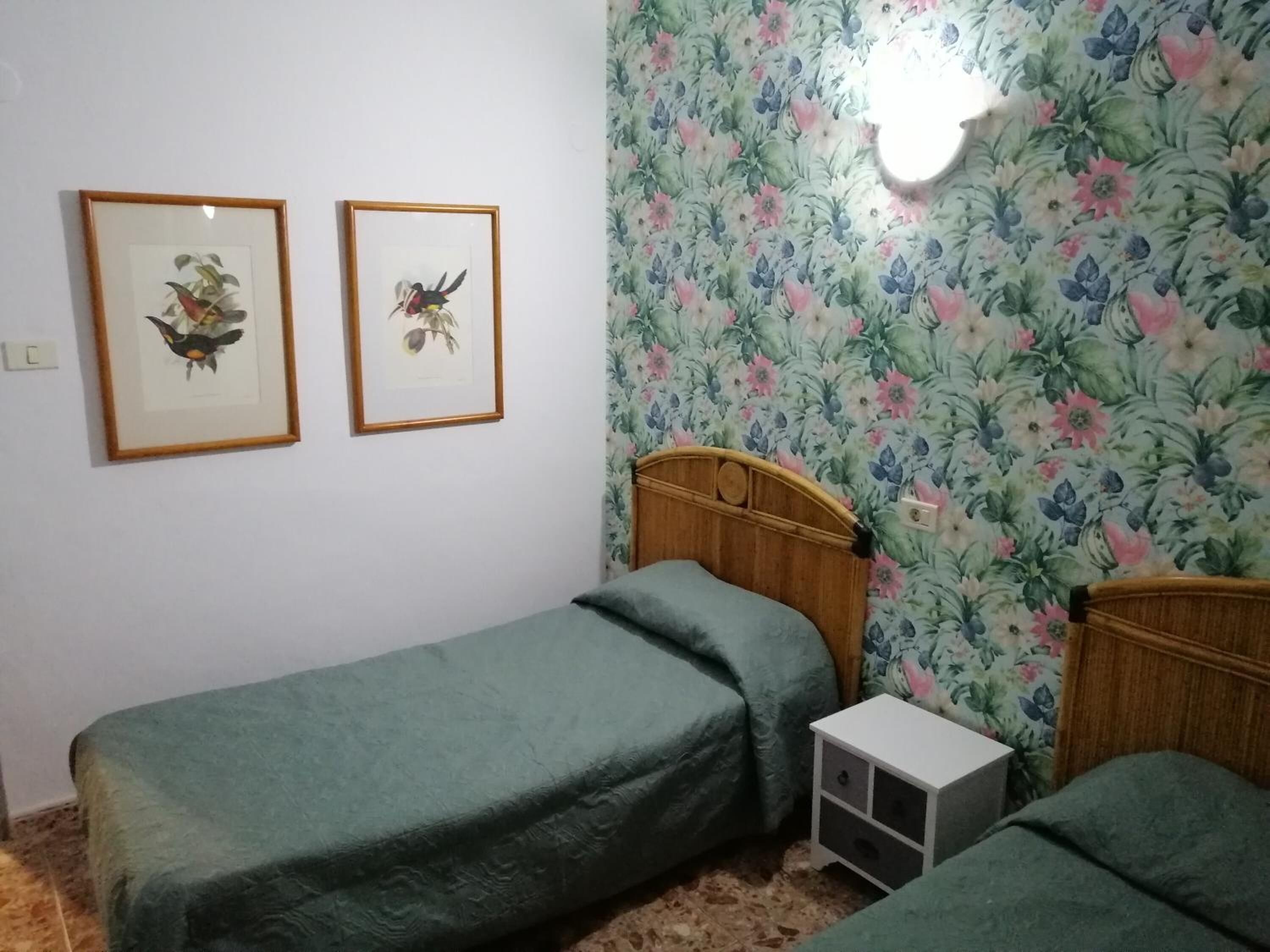 A room with two single beds, a small bedside table, and floral wallpaper.