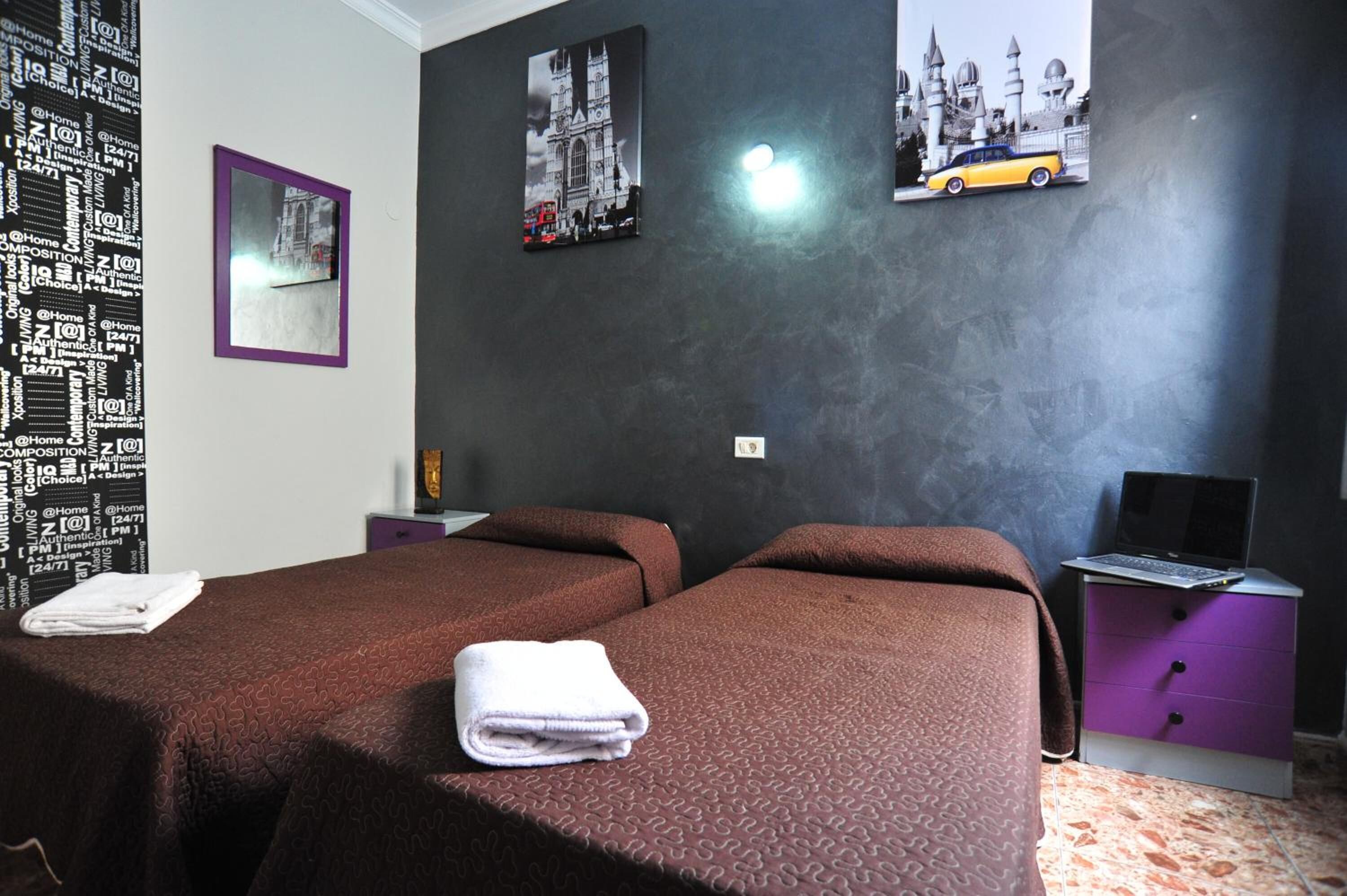 A hotel room with two beds, a desk with a laptop, and a wall with framed pictures.