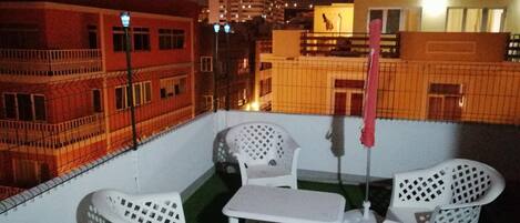 Une terrasse sur le toit, avec des chaises en plastique blanc et une petite table, le tout entouré d’une clôture blanche.