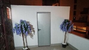 Una puerta blanca con un picaporte negro, flanqueada por dos macetas con flores moradas.