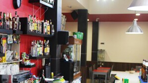 Zona de bar con estantes llenos de botellas de licores, una máquina de café y un letrero que dice 'Tropical'.