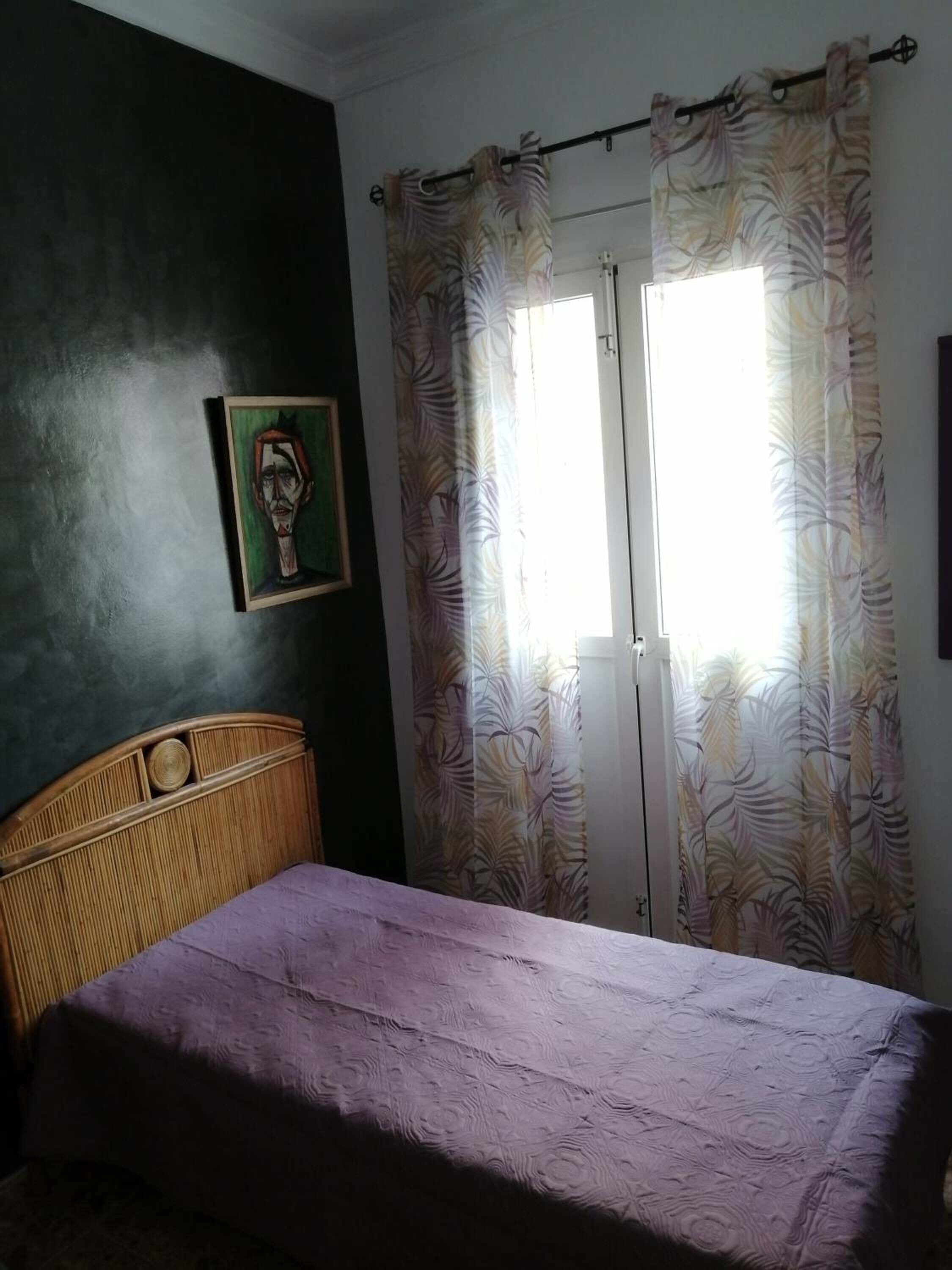 Um quarto com cama, cabeceira, um quadro na parede e janela com cortinas.