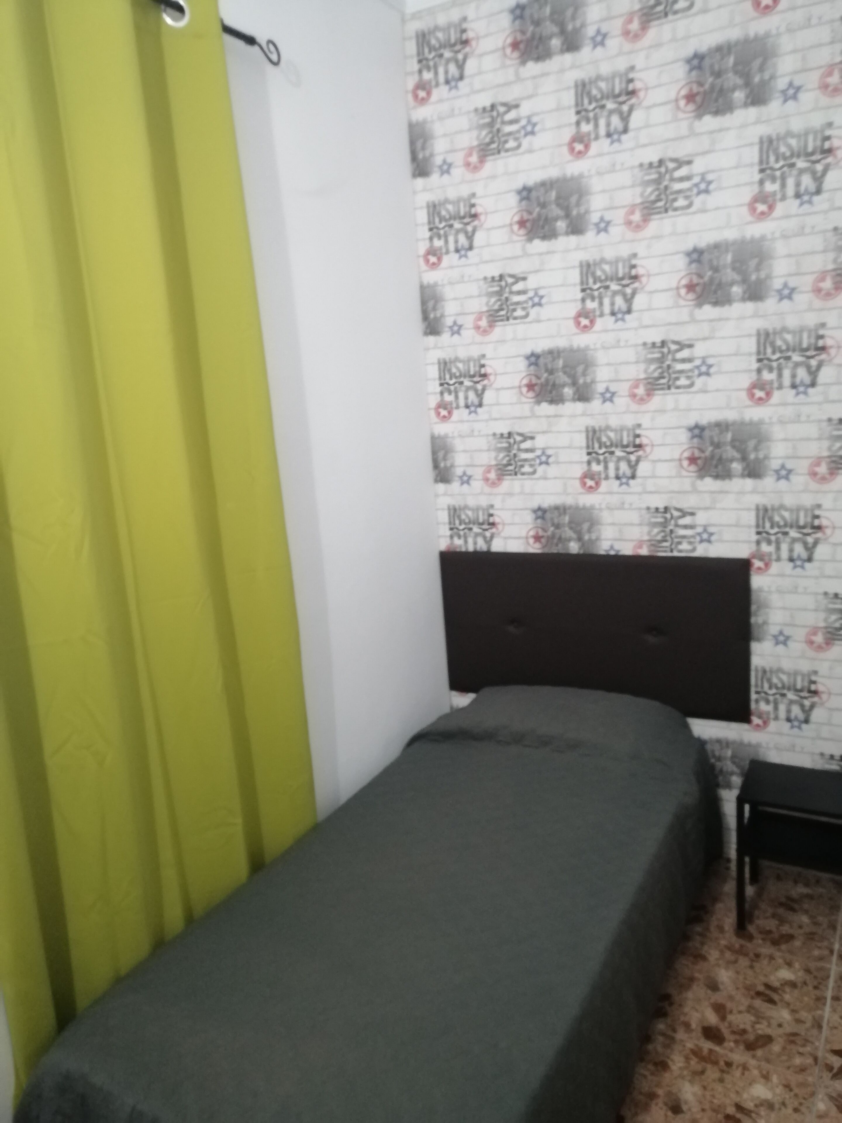 A room with a bed, a green curtain, a patterned wallpaper, and a dark headboard.