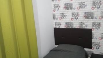 A room with a bed, a green curtain, a patterned wallpaper, and a dark headboard.