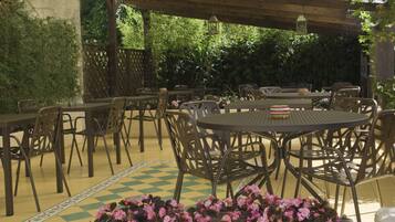 Un patio al aire libre con varias mesas y sillas, rodeado de follaje y un diseño decorativo en el suelo.
