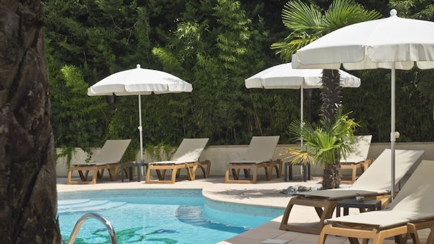 A pool area with lounge chairs and umbrellas, surrounded by greenery. - Les Oliviers (Fayence)