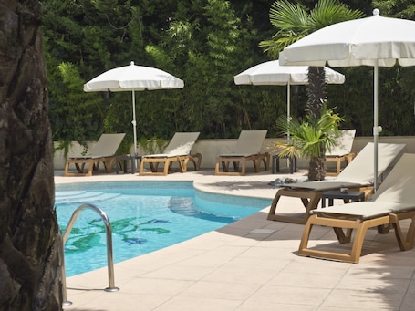 A pool area with lounge chairs and umbrellas, surrounded by greenery.