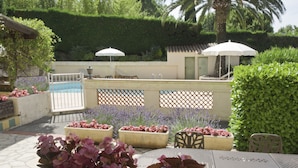 An outdoor patio with seating, planters with flowers, and a pool area. - Les Oliviers (Fayence)