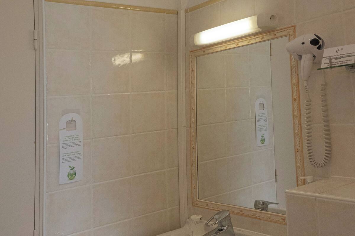 Ein Badezimmer mit Waschbecken, Spiegel, Handtuchhalter und einem an der Wand befestigten Föhn.