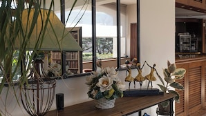 A room with a wooden table, a lamp, a vase with flowers, and a shelf with figurines. - Les Oliviers (Fayence)