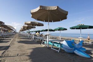 A beach with rows of sun umbrellas and lounge chairs, a lifeguard tower, and a shark float. - Canado Family Hotel (Castagneto Carducci)