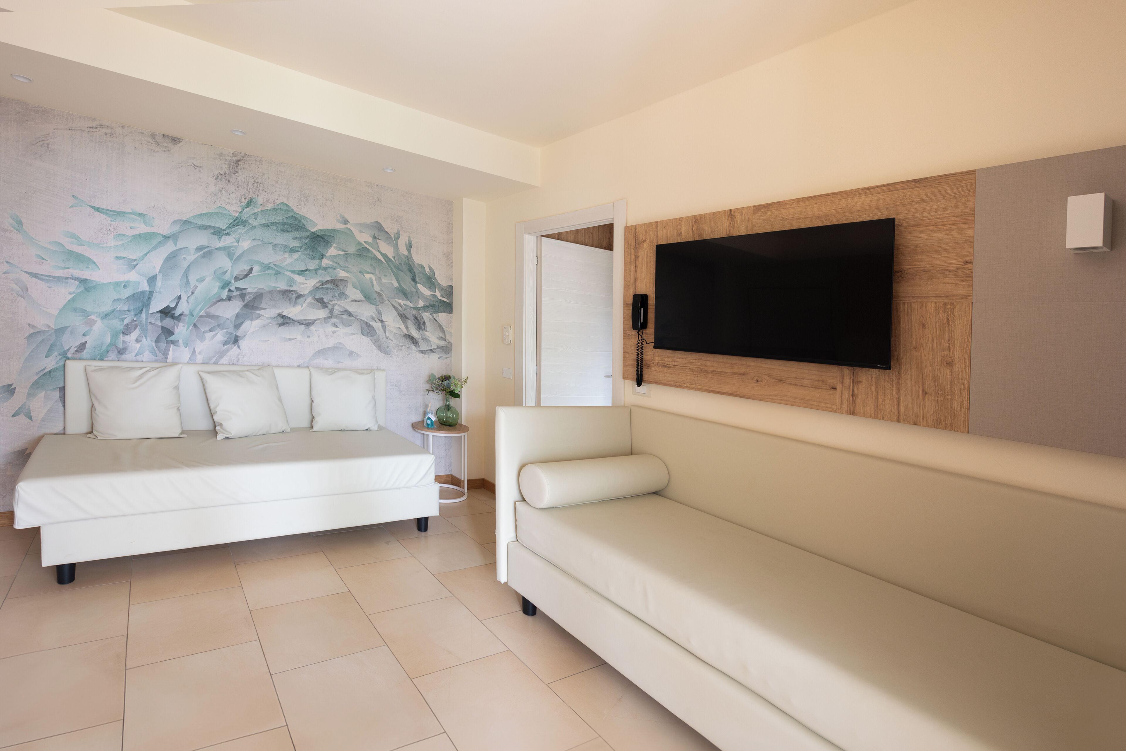 A modern hotel room with a large bed, a sofa, a flat-screen TV mounted on the wall, and a decorative wall mural.