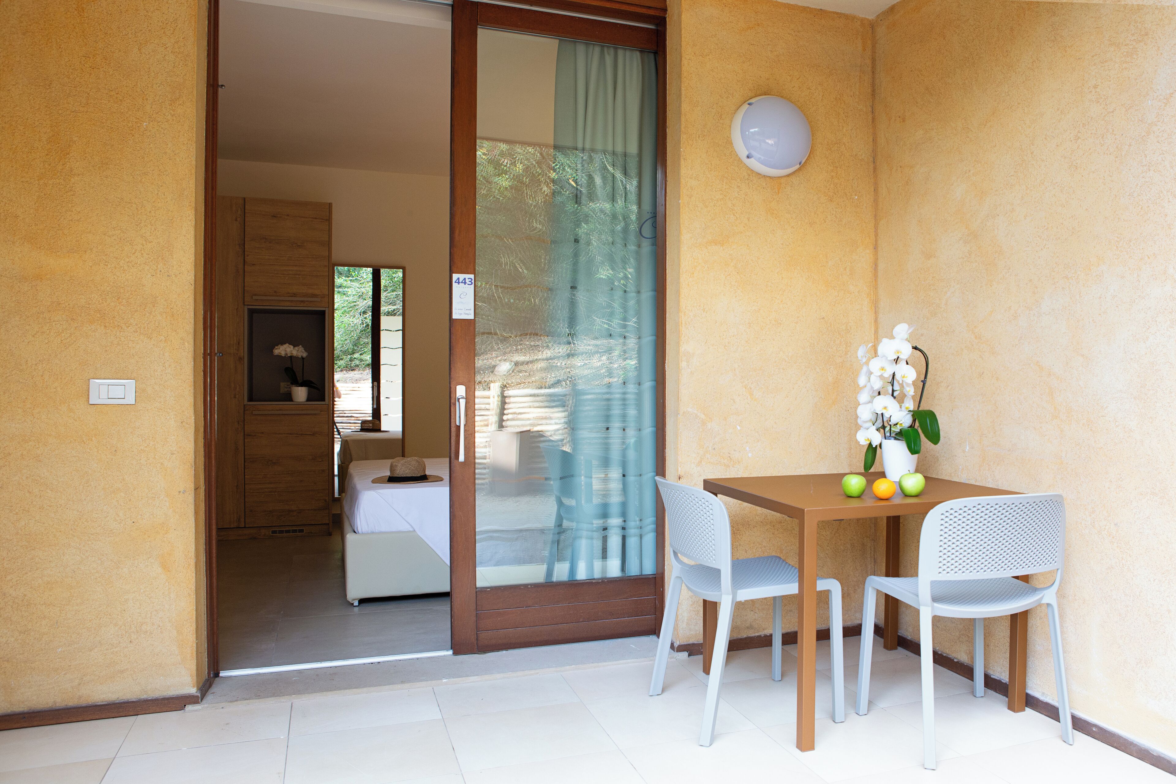 Ein Zimmer mit Holztür, einem kleinen Tisch mit zwei Stühlen und einer Topforchidee.
