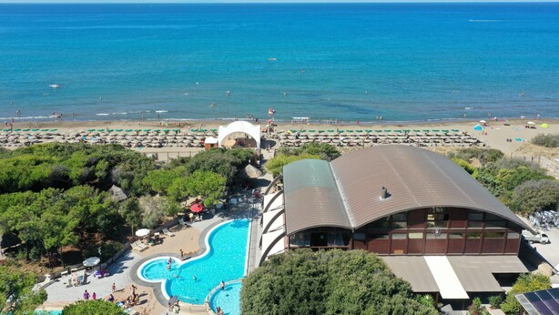 Ein Resort mit großem Schwimmbad, Strandbereich und einem Gebäude mit gewölbter Dachform.
