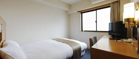 A hotel room with a bed, a desk with a television, and an air conditioning unit.