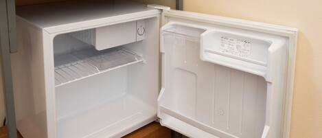 A compact refrigerator with a freezer compartment, located in a kitchen with a wooden countertop and a metal shelf above.