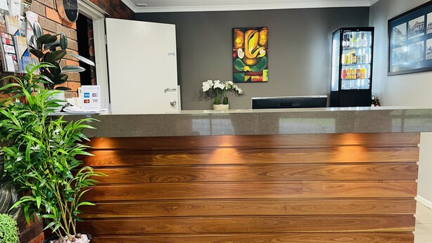Un área de recepción con mostrador de madera, una planta en maceta, un reloj de pared y un refrigerador.