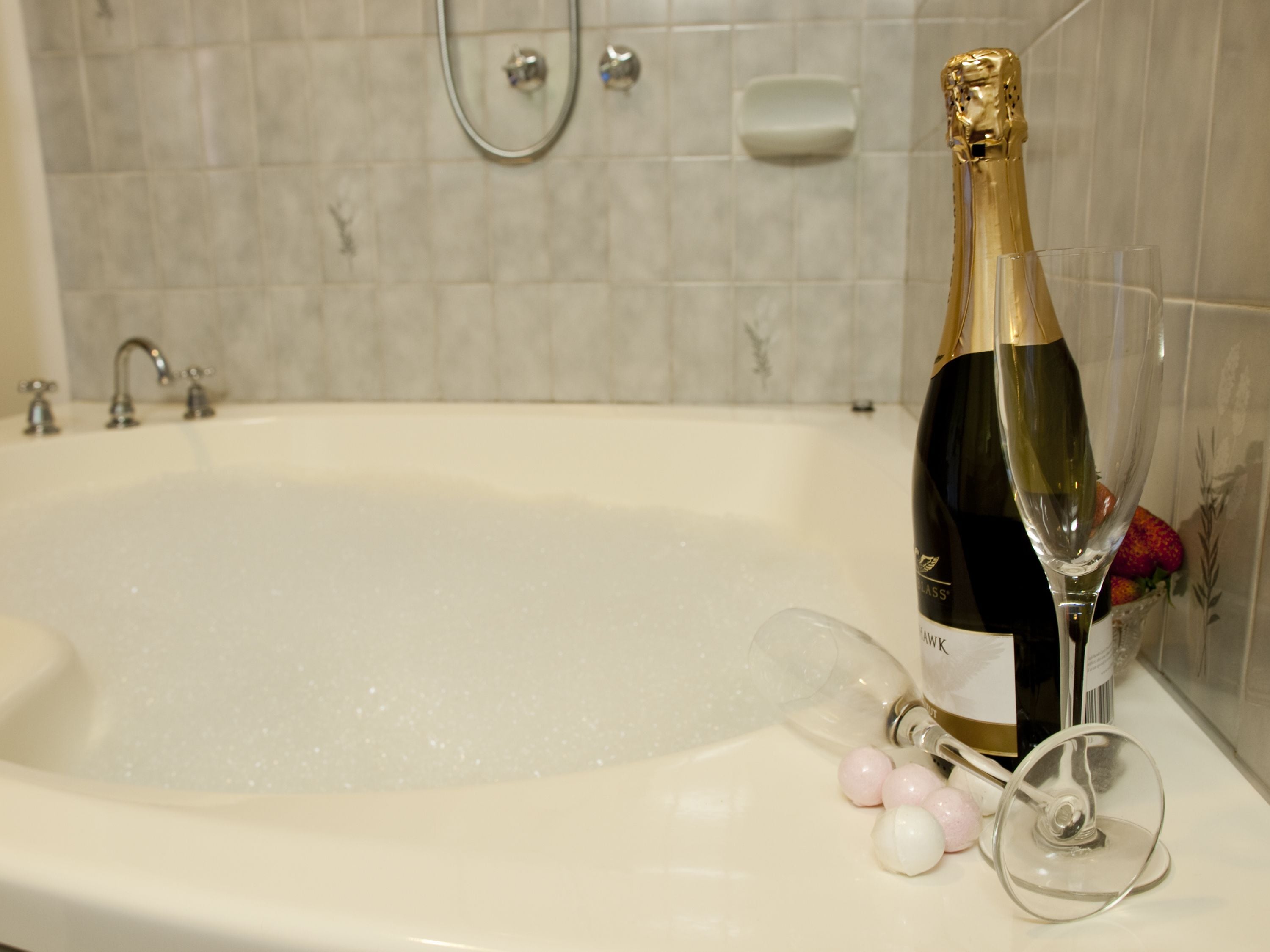 A champagne bottle in a bathtub with a showerhead and soap dish in the background.