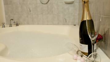 A champagne bottle in a bathtub with a showerhead and soap dish in the background.