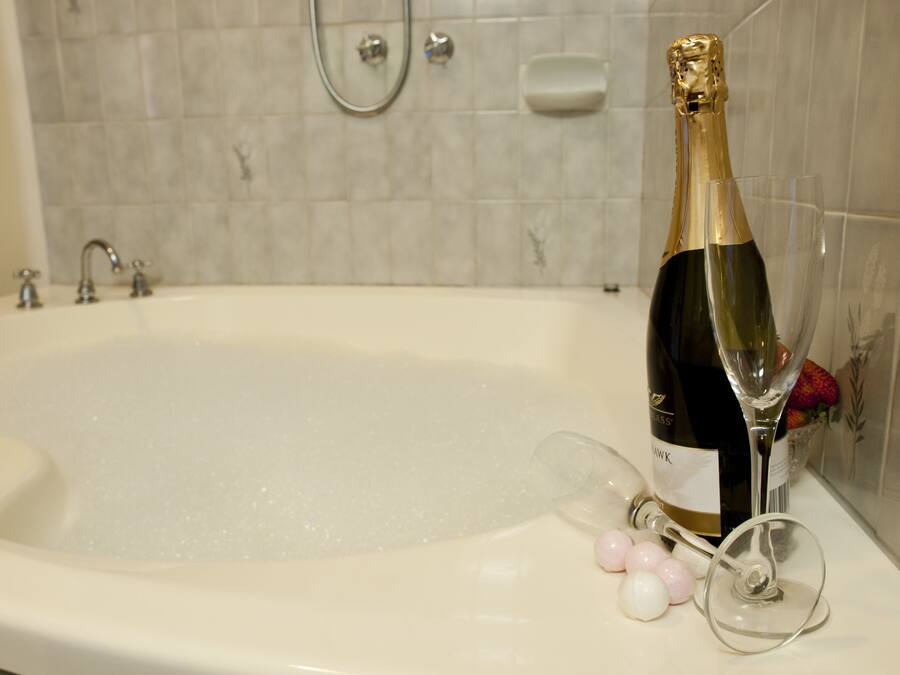 A champagne bottle in a bathtub with a showerhead and soap dish in the background.