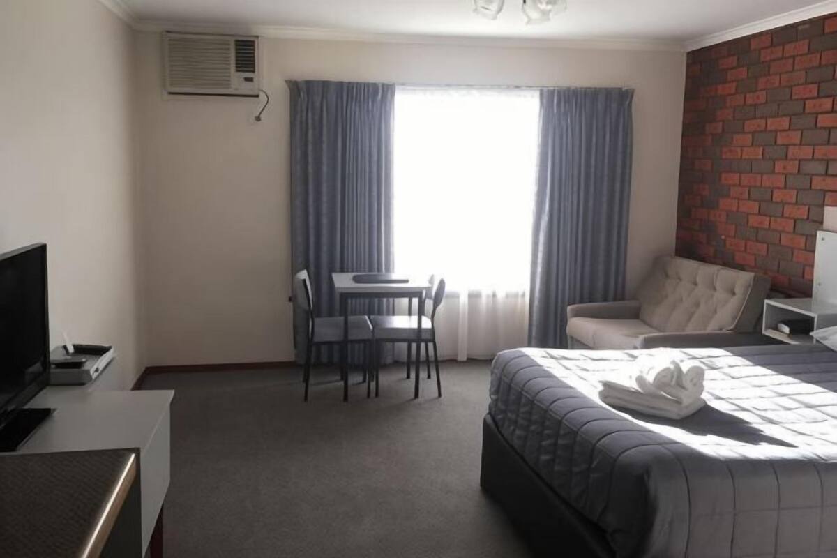 A hotel room with a bed, a desk, a chair, a television, and a window with curtains.