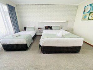 Ein Hotelzimmer mit zwei Betten, einer weißen Ziegelwand, einem Fenster mit Vorhängen und einem Bild an der Wand.