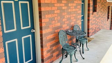 Een gebouw met een blauwe deur waarop het cijfer 2 staat, bakstenen muren en twee sierlijke metalen stoelen op een betonnen vloer.