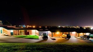 Edificio residencial de noche con varios autos estacionados y ventanas iluminadas.
