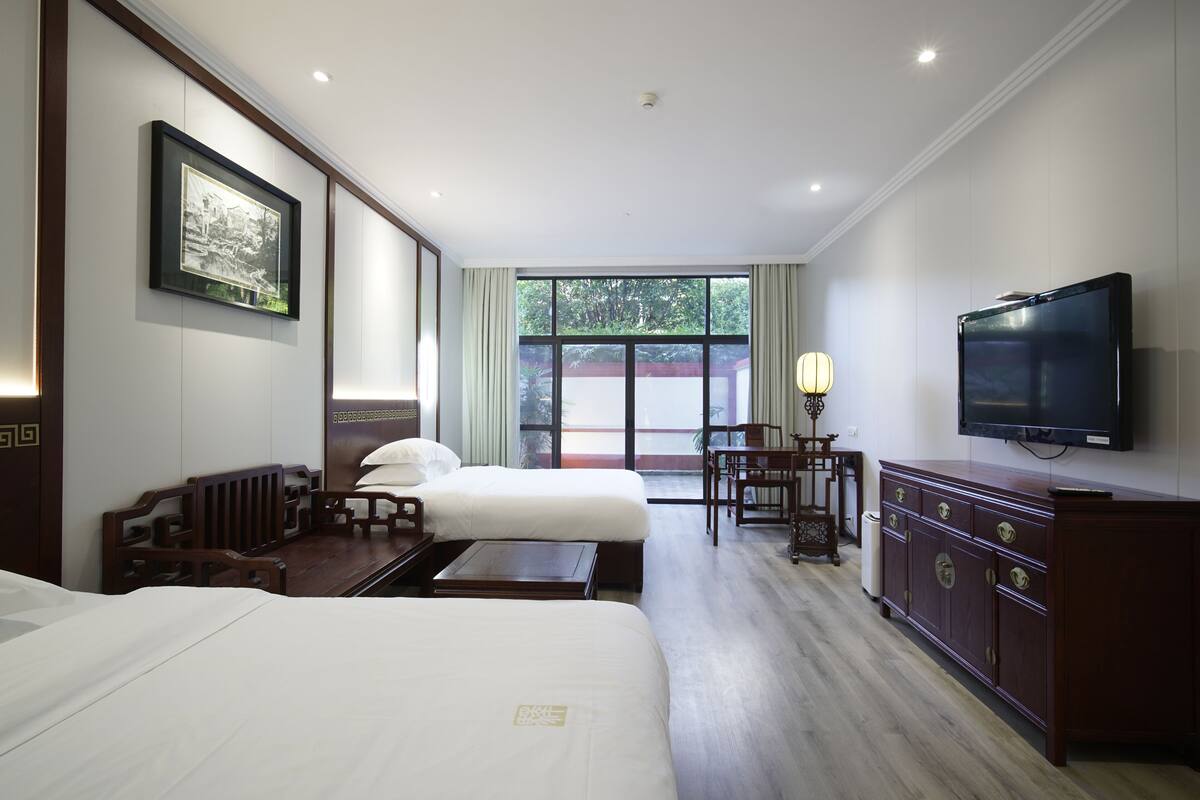 A hotel room with two beds, a TV, a desk, and a window with a view.
