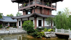 Un edificio tradicional de varios pisos con tejado de tejas y balcones, un estanque con peces koi y un pequeño puente.
