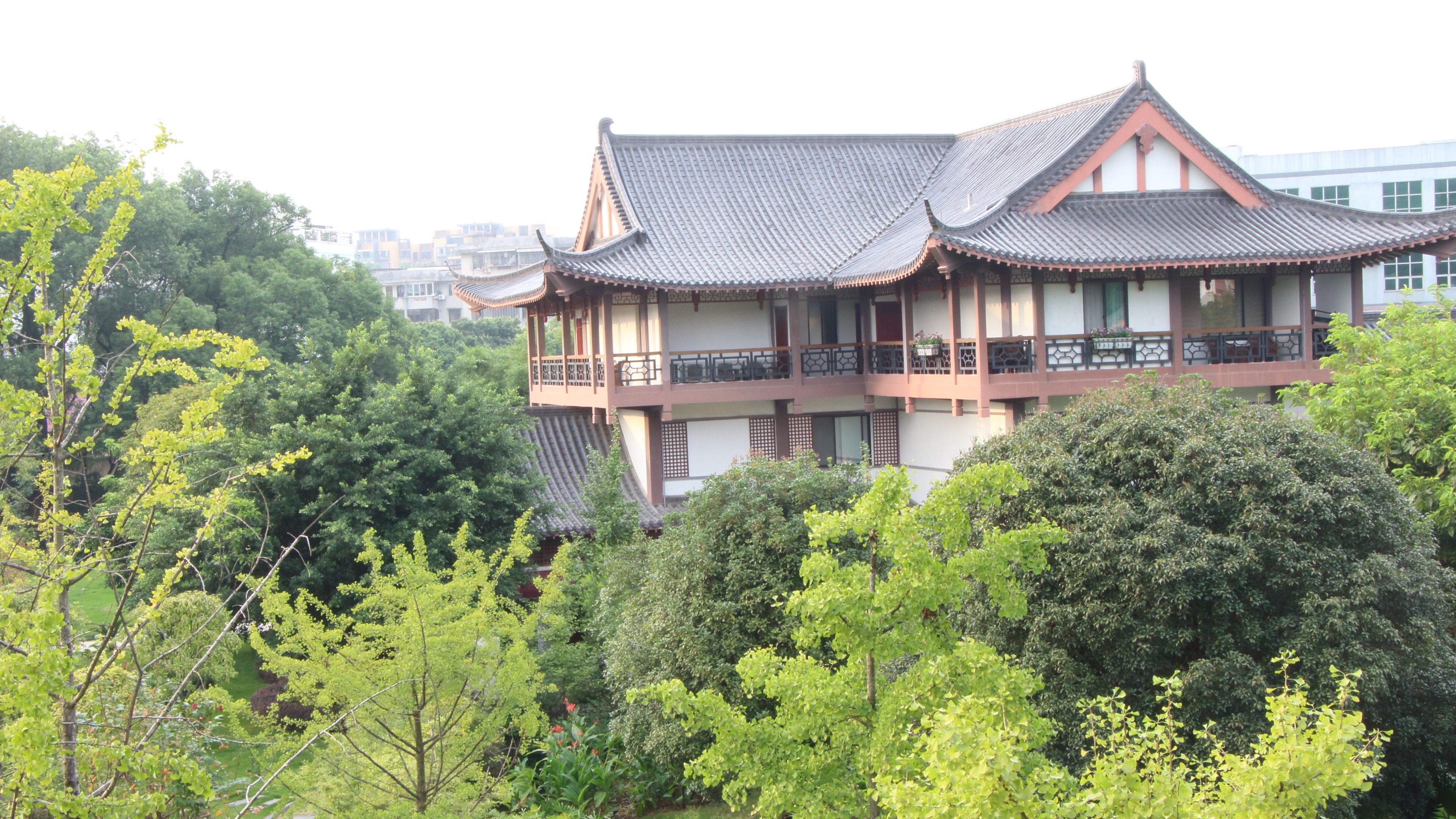 A traditional building with multiple floors, balconies, and a tiled roof, surrounded by lush greenery.