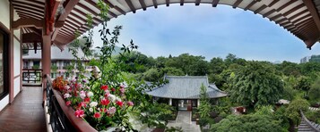 A traditional building with a tiled roof, surrounded by lush greenery and a balcony with flowers.
