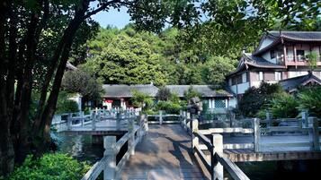 A traditional wooden bridge over a calm water body, surrounded by lush greenery and traditional buildings with tiled roofs.