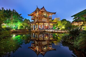 A traditional two-story building with a reflection in the water, surrounded by lush greenery and a small bridge.