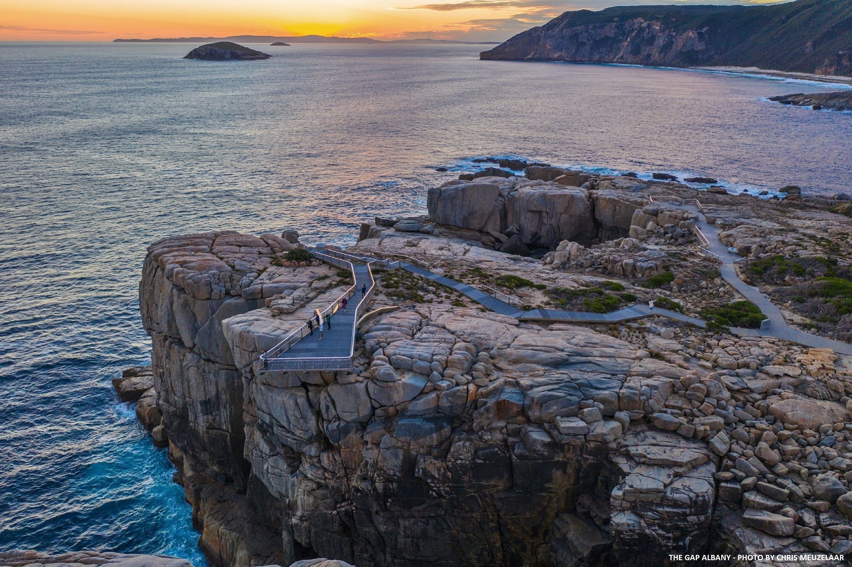 Un acantilado costero con un sendero que lleva a un mirador con vistas al mar.