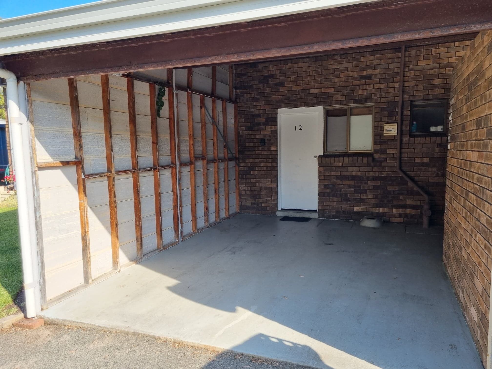 A garage with a brick wall, a white door marked with the number 12, and a small window.