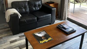 Una sala de estar moderna con un sofá de cuero negro, una mesa de centro de madera, un cuadro enmarcado en la pared y un televisor sobre el sofá.