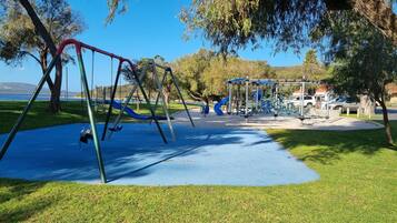 A playground with swings and slides, surrounded by grass and trees, with a clear view of the sky.