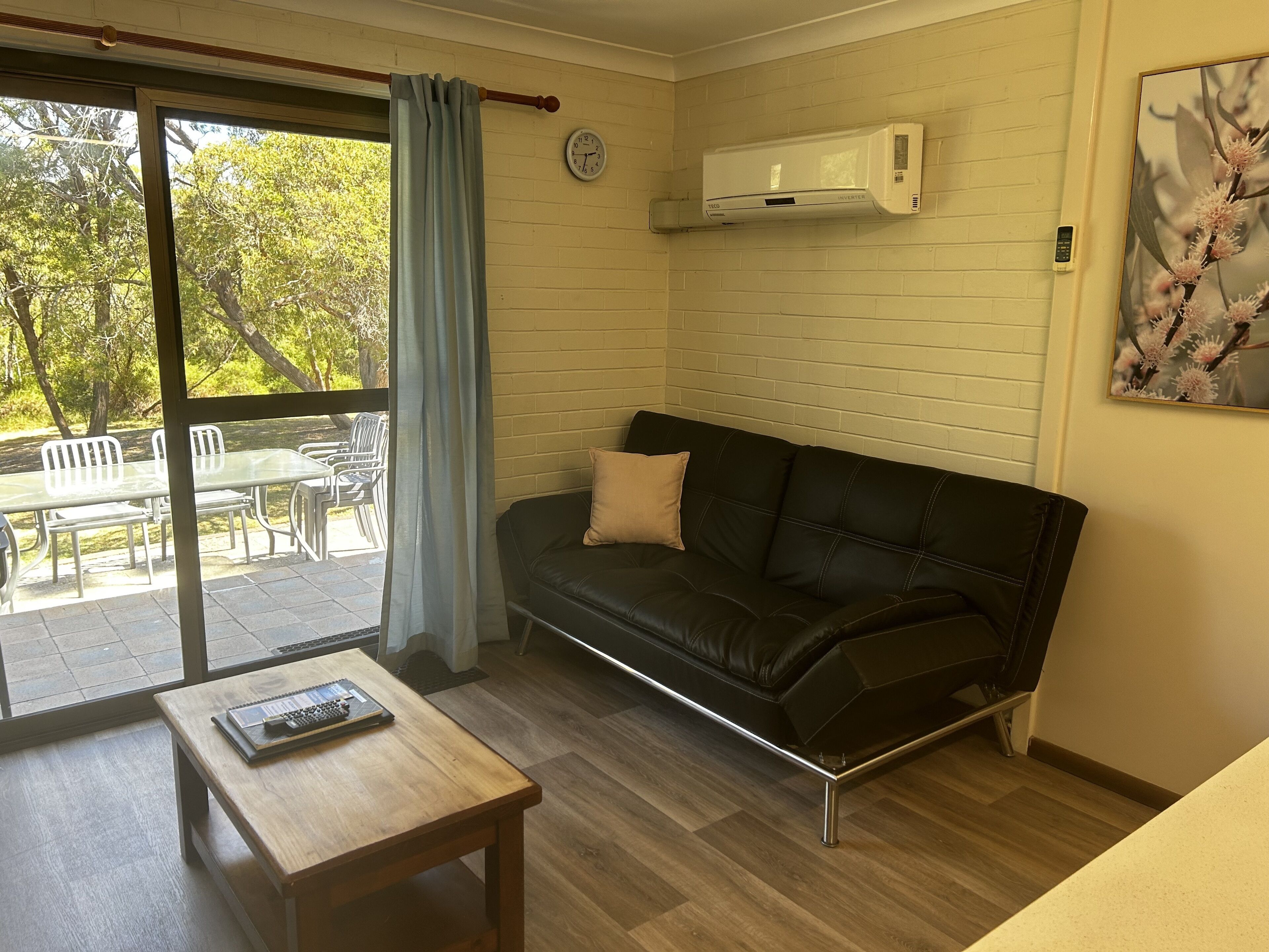 Una sala moderna con un sofá de cuero negro, una mesa de centro de madera y un ventanal corredizo que da a un patio exterior.
