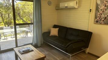 Una sala moderna con un sofá de cuero negro, una mesa de centro de madera y un ventanal corredizo que da a un patio exterior.