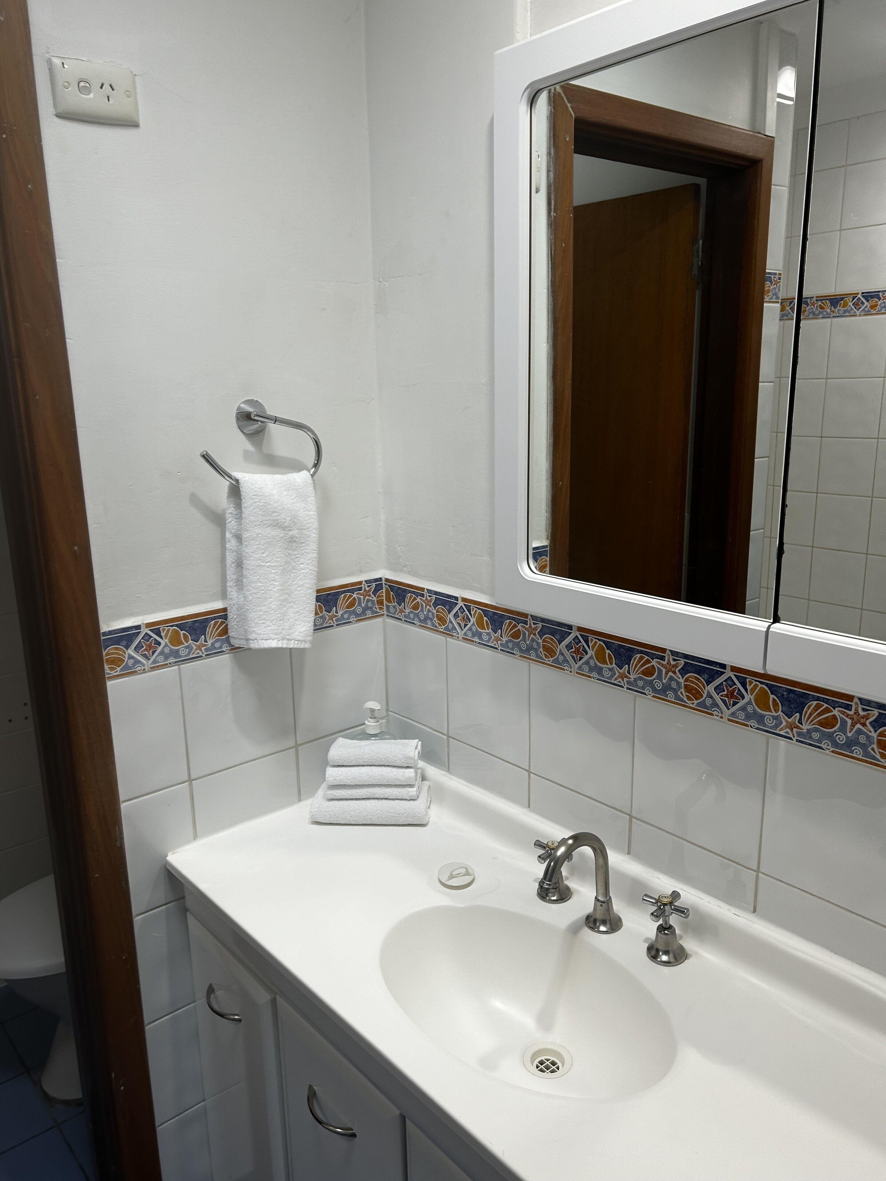Un baño con un lavamanos blanco, un espejo y un perchero para toallas.